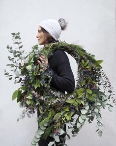 a woman wearing a hat and scarf holding a wreath with greenery around her neck