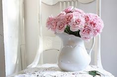 a white vase filled with pink flowers on top of a lace tablecloth covered table