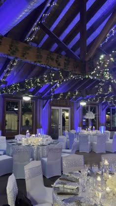 an indoor wedding venue with white linens and blue uplighted ceilinging, decorated with fairy lights