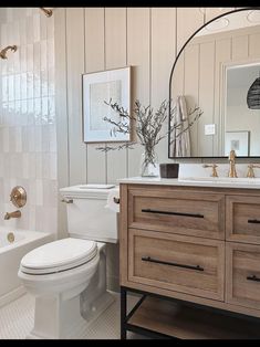 a white toilet sitting next to a bath tub in a bathroom under a mirror on top of a wooden cabinet