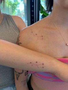 two women with tattoos on their chests and one has her arm wrapped around the other