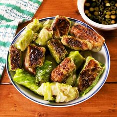 a white plate topped with lettuce and meat next to a bowl of olives