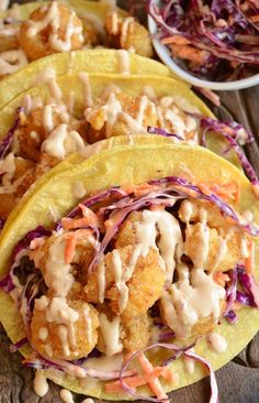 three tacos filled with meat and coleslaw on top of a wooden table