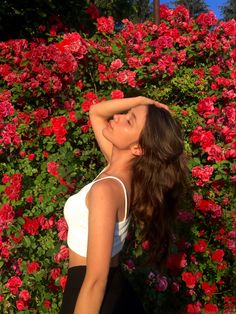 a woman standing in front of flowers with her arms behind her head and eyes closed