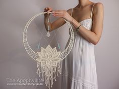 a woman in white dress holding up a dream catcher with beads hanging from it's sides