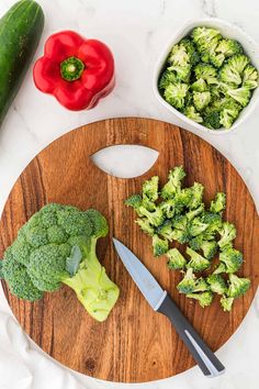 a cutting board with broccoli, peppers and cucumbers next to it