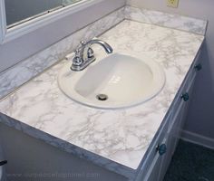 a white sink sitting under a bathroom mirror on top of a counter next to a window