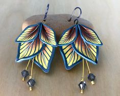 two pairs of earrings with yellow and blue leaves hanging from it's sides on top of a rock