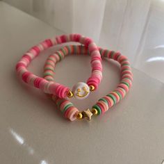 two bracelets with colorful beads are sitting on a white counter top, one has a button and the other has a smiley face