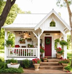 a small white house with potted plants on the front porch and red door, surrounded by greenery