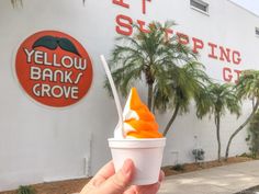 a person holding up a cup filled with orange and white ice cream in front of a building