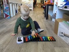 a little boy sitting on the floor playing with a colorful toy that looks like a piano