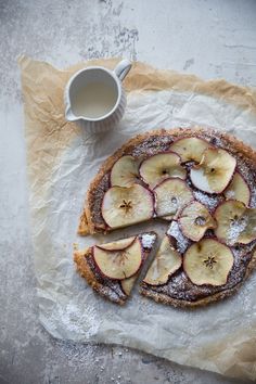 an apple tart with slices cut out on parchment paper next to a cup of coffee