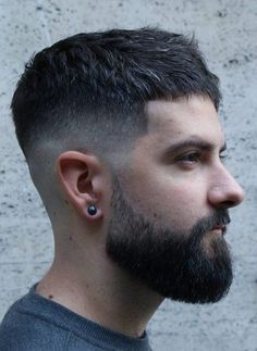 a close up of a man with a beard and piercings on his ears looking off to the side