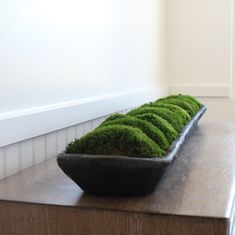 a black bowl filled with green moss sitting on top of a wooden table next to a white wall