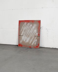 a painting on the ground in front of a white wall with graffiti written on it