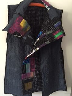 a black vest with multicolored patches on the front and back, hanging up against a white wall