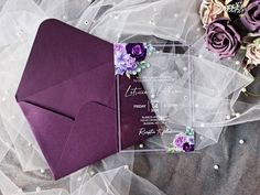 a purple and white wedding stationery on top of a veiled table cloth with flowers