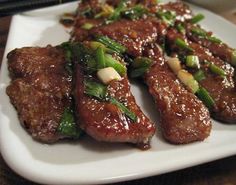 some meat and vegetables are on a white plate with chopsticks next to it