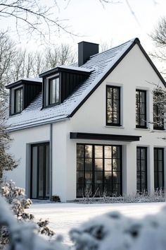 a white house with black windows and snow on the ground