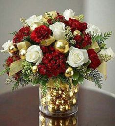 a vase filled with red and white flowers sitting on top of a table next to gold ornaments