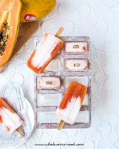 two popsicles are on a tray next to some bananas and papaya slices in the background