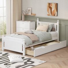 a white bed with drawers underneath it in a room next to a rug and window