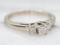 This diamond ring is simple in concept but features beautiful little details including the two small accent diamonds on the shoulders of the ring. The center stone in this vintage piece is a princess-cut diamond, a gemstone with an intense fire that shimmers on the finger with classic elegance! Metal: 14K White Gold Gem: Diamond .12 Carats, VS2 in Clarity, H in Color Gem Measurements: 2.7 mm, Princess Cut Accents: 2 Diamonds totaling .13 Carats, SI2 in Clarity, G-H in Color Ring Size: 5.75 Marks: "14K" Stamped on the inside band Moissanite Wedding Set, European Cut Diamond Ring, 14k White Gold Diamond Ring, Three Stone Diamond Rings Engagement, Filigree Engagement Ring, Three Stone Diamond Ring, Diamond Engagement Wedding Ring, Three Stone Diamond, Sapphire Engagement Ring Blue