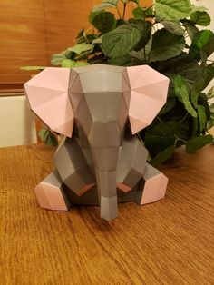 an origami elephant sitting on top of a wooden table next to a potted plant