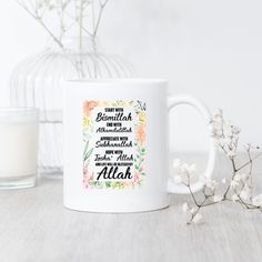 a white coffee mug sitting on top of a table next to a vase with flowers