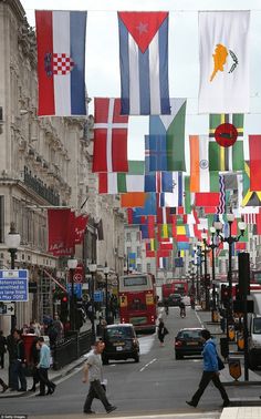 many flags are flying in the air on a city street with cars and people walking