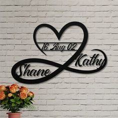 two hearts with names are on the wall next to a potted plant and vase