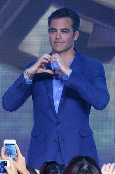 a man in a blue suit is holding his hands up to the side as people take pictures