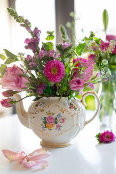 a tea pot with flowers in it sitting on a table next to other vases