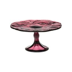 a pink glass cake plate sitting on top of a white table with an intricate design