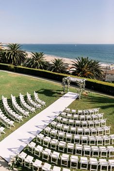 an outdoor ceremony setup with white chairs on the lawn and ocean in the back ground