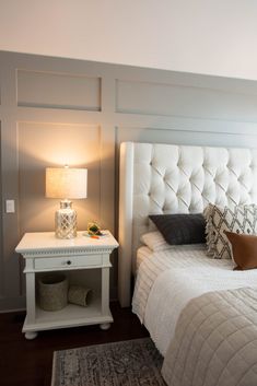 a white bed sitting in a bedroom next to a nightstand with a lamp on it