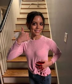 a woman standing in front of stairs giving the thumbs up sign with blood on her shirt