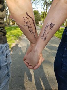 two people holding hands with tattoos on their arms