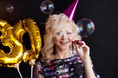 a woman wearing a party hat and blowing bubbles on her face while standing in front of balloons