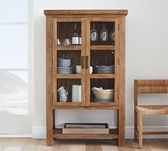 a wooden cabinet sitting next to a chair in a room with white walls and wood flooring