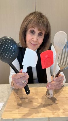 a woman holding up several spatulas and spoons