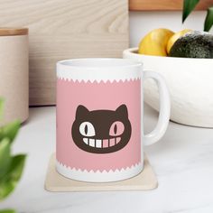 a pink and white coffee mug with a black cat's face on it