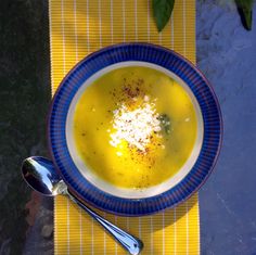 a blue and white bowl filled with soup on top of a yellow place mat next to a spoon