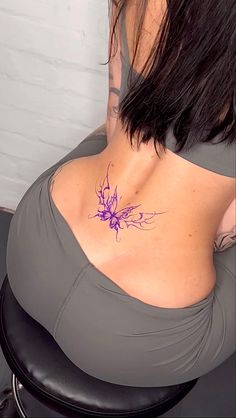 the back of a woman's stomach with a tattoo on her left side and purple flowers