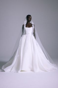 a woman in a white wedding dress with a veil on her head, standing against a gray background