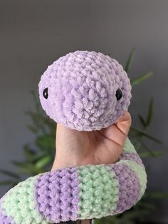 a hand holding up a purple and green crocheted snake toy with black eyes