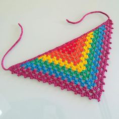 a crocheted triangle is hanging on a white surface with pink string and beads