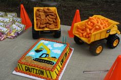 there is a birthday cake with construction trucks on it and orange cones in the background