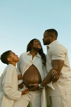 three people standing next to each other with their hands on the belly of a pregnant woman